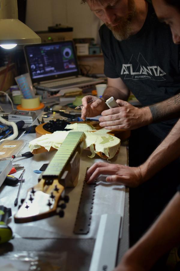 Photo dans l'atelier jérôme le formateur apprend à Juliano le le recrownage des frettes