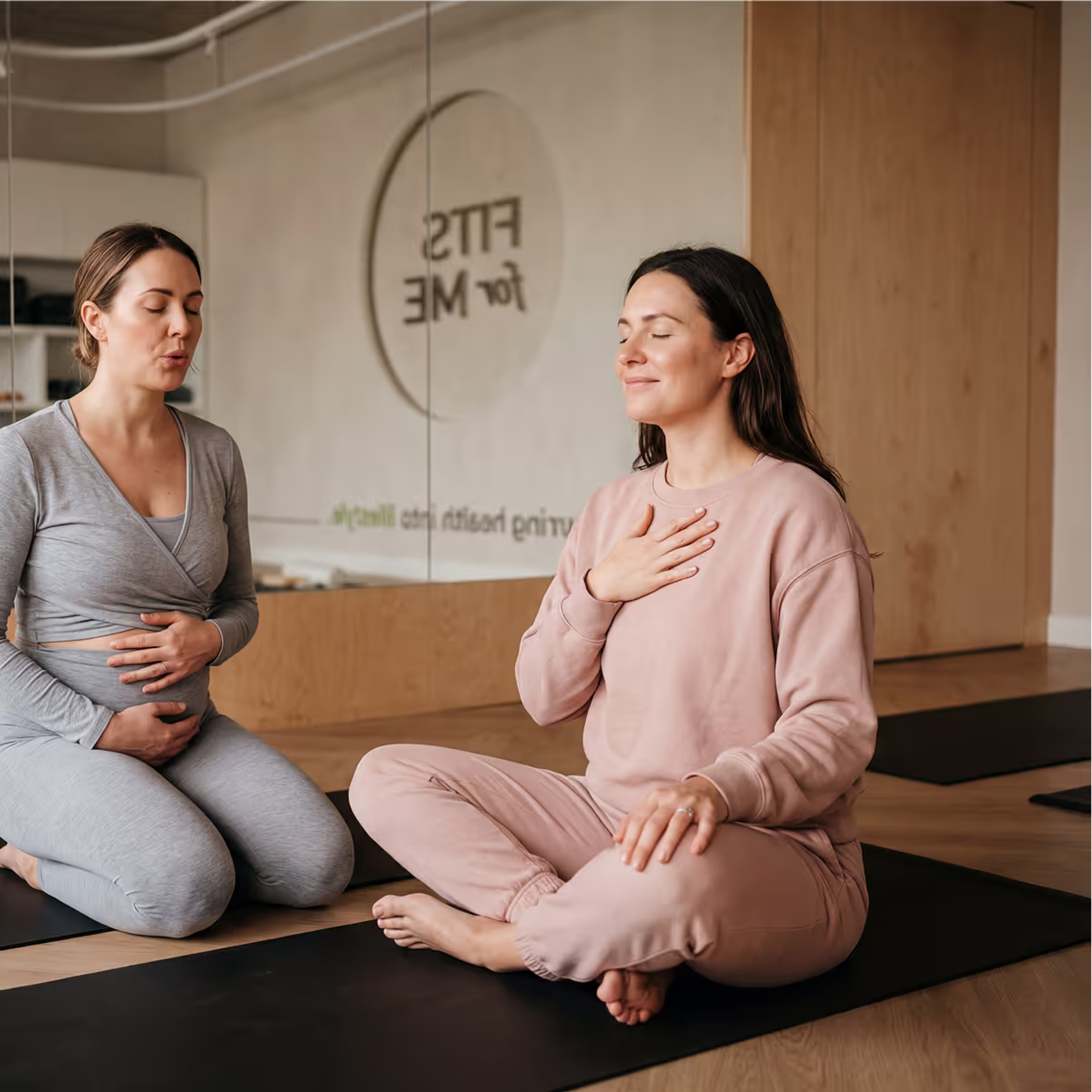 Two women seated on the floor, one resting a hand on her chest while breathing