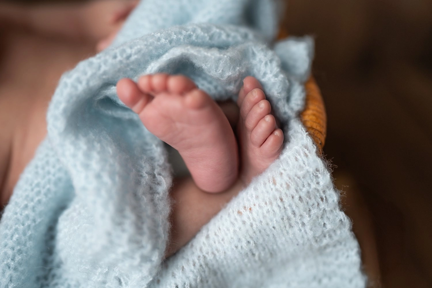 Zwei kleine Babyfüße schauen unter einer weichen blauen Strickdecke hervor.