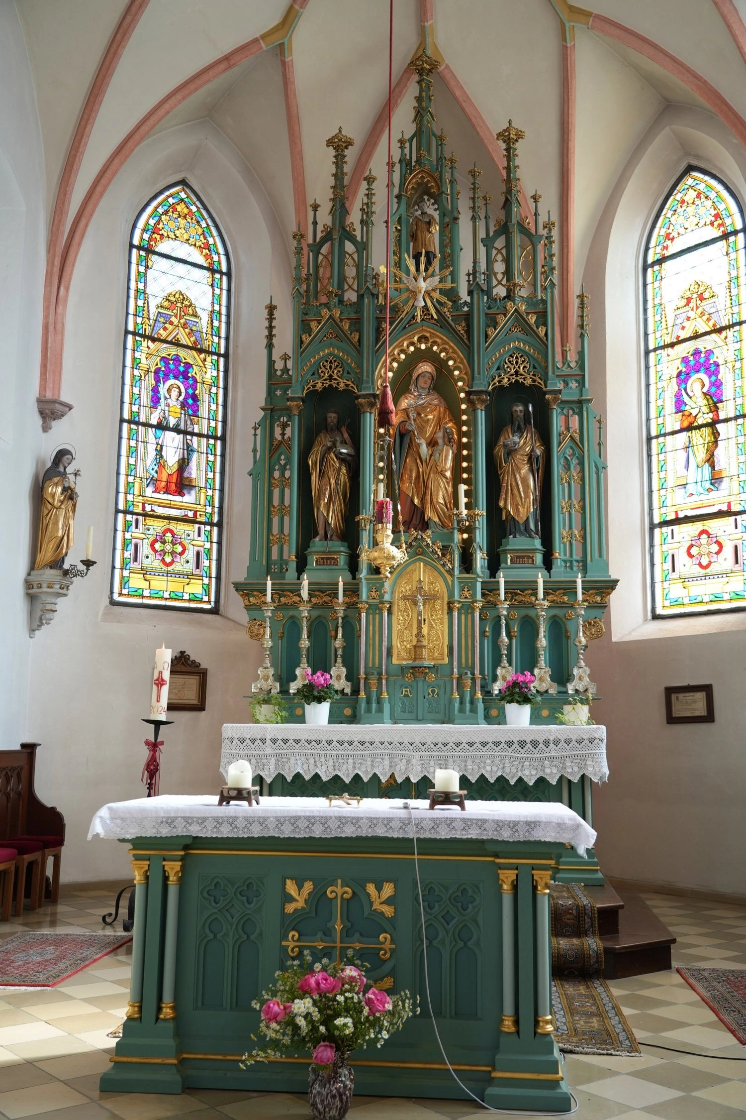 Ein Kirchenaltar steht hinter dem Taufbecken zwischen bunten hohen Fenstern.
