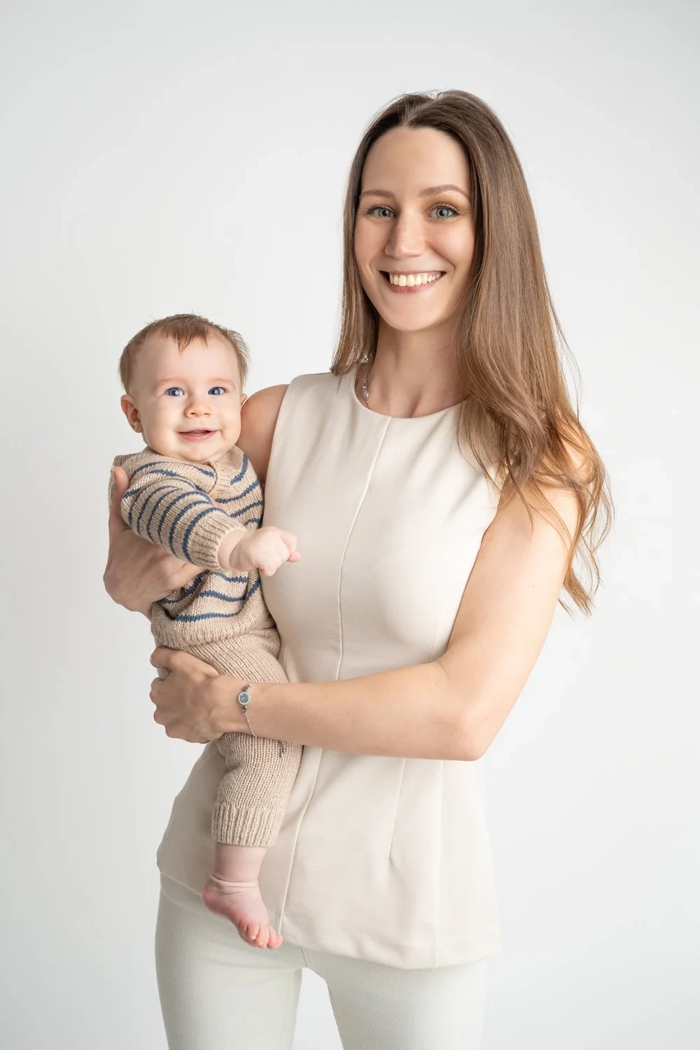 Eine lächelnde Frau in heller Kleidung hält ihr Baby im Arm.