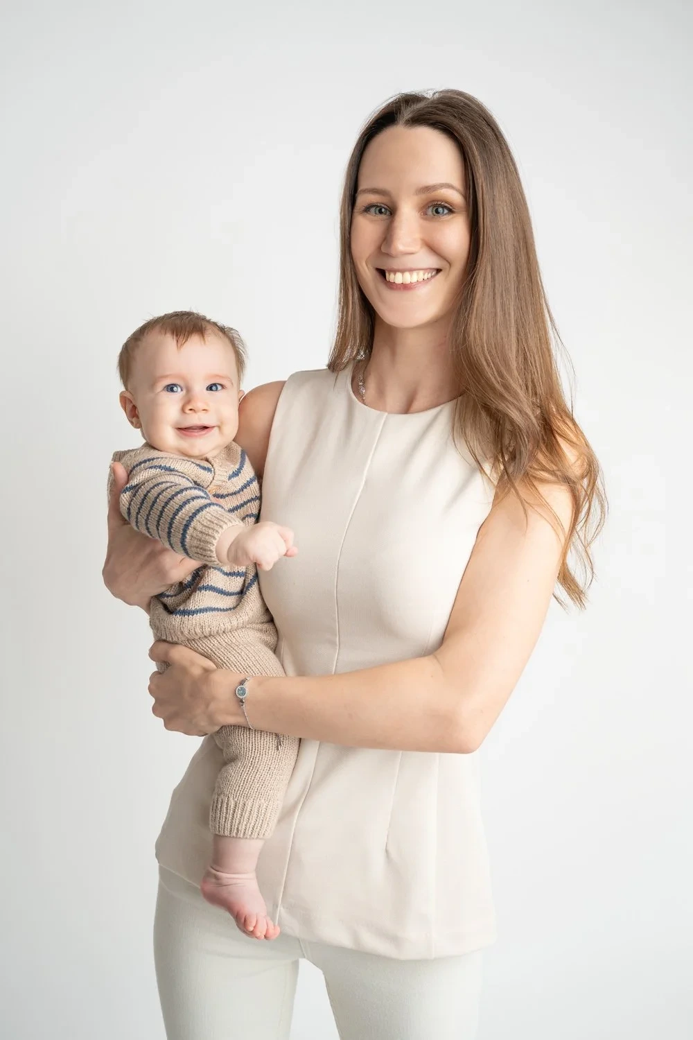 Eine lächelnde Frau in heller Kleidung hält ihr Baby im Arm.