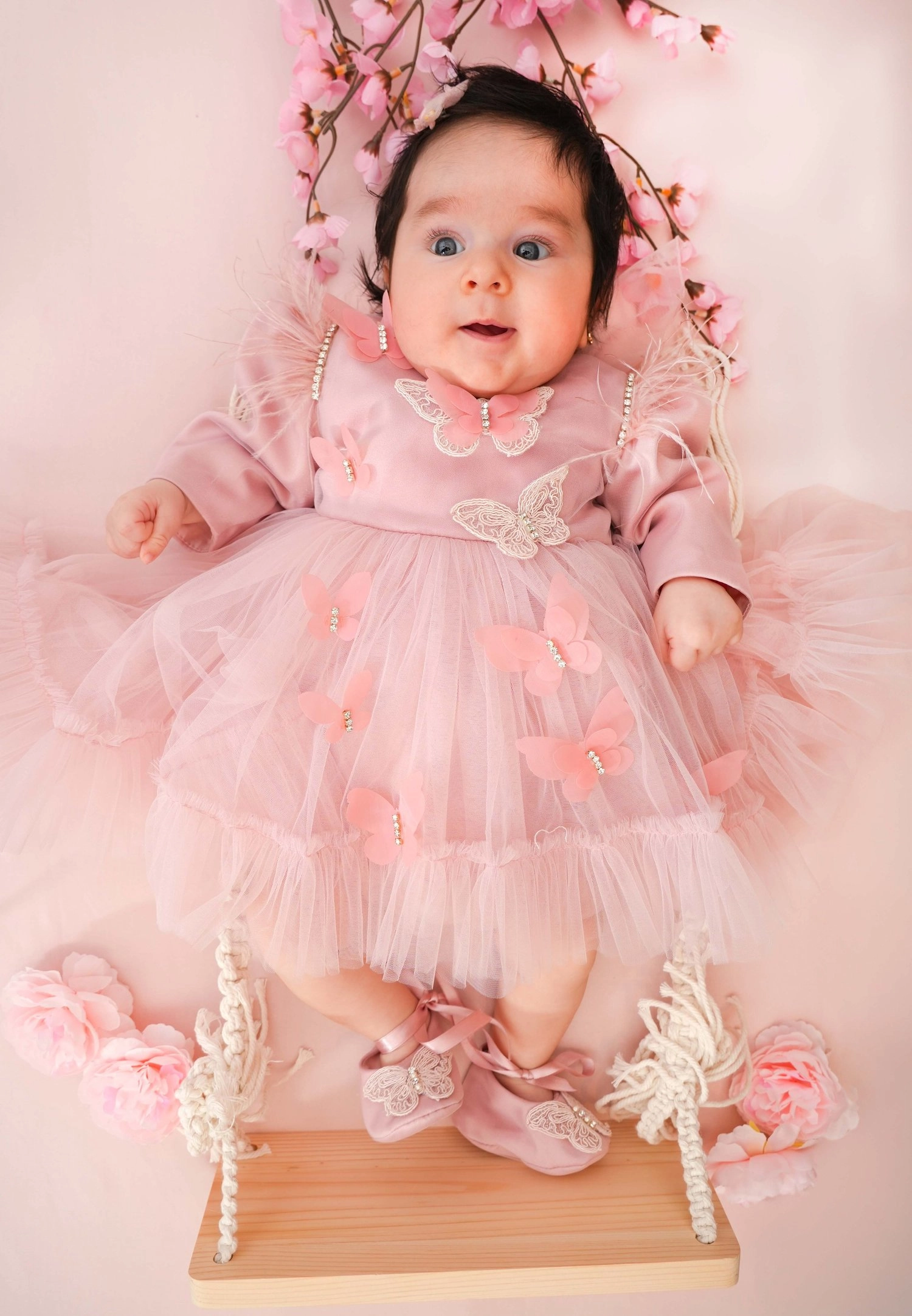 Ein Baby im rosa Kleid liegt zwischen zarten rosa Blüten.