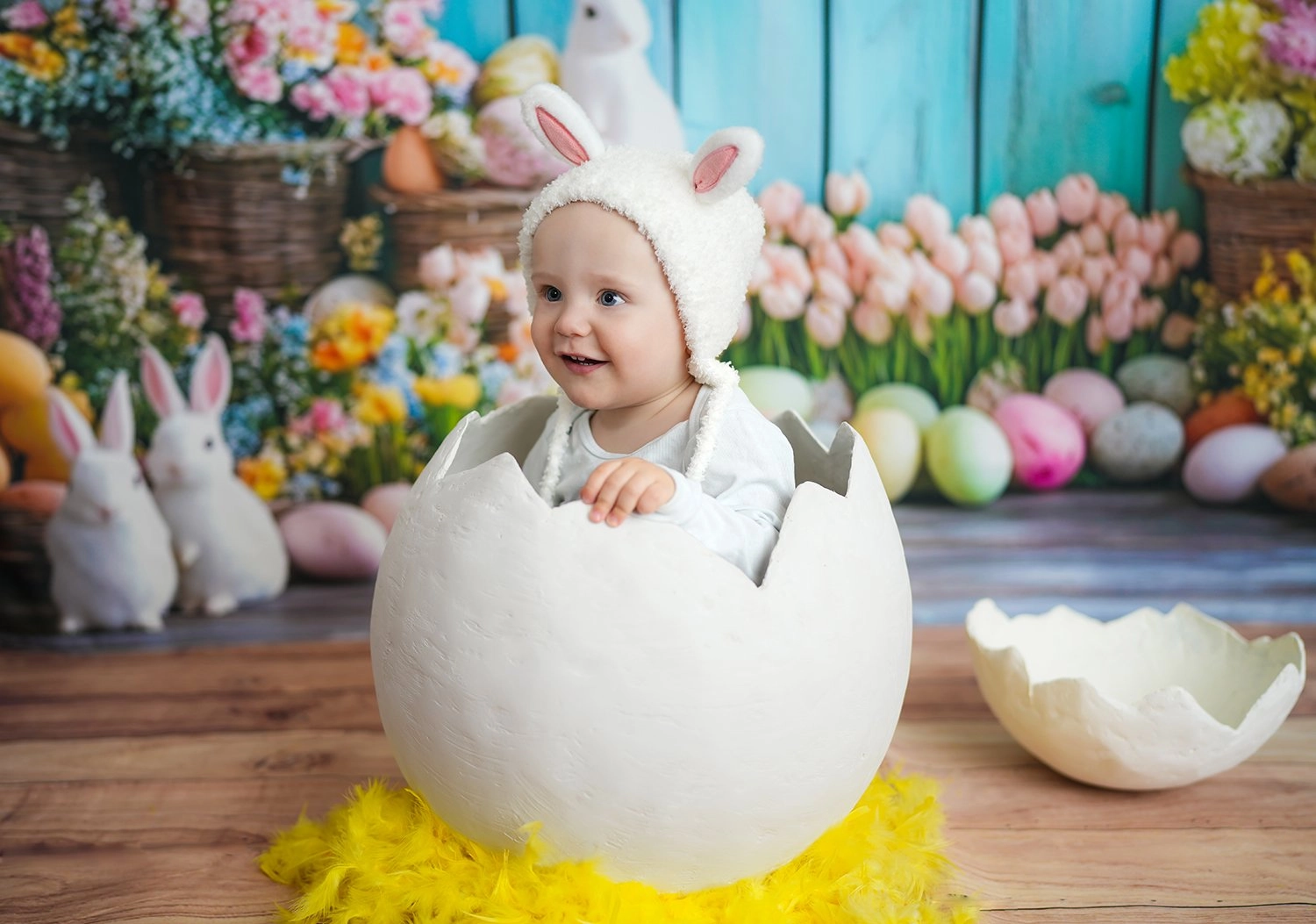 Ein lachendes Baby mit Hasenmütze sitzt in einem großen weißen Dekoei.