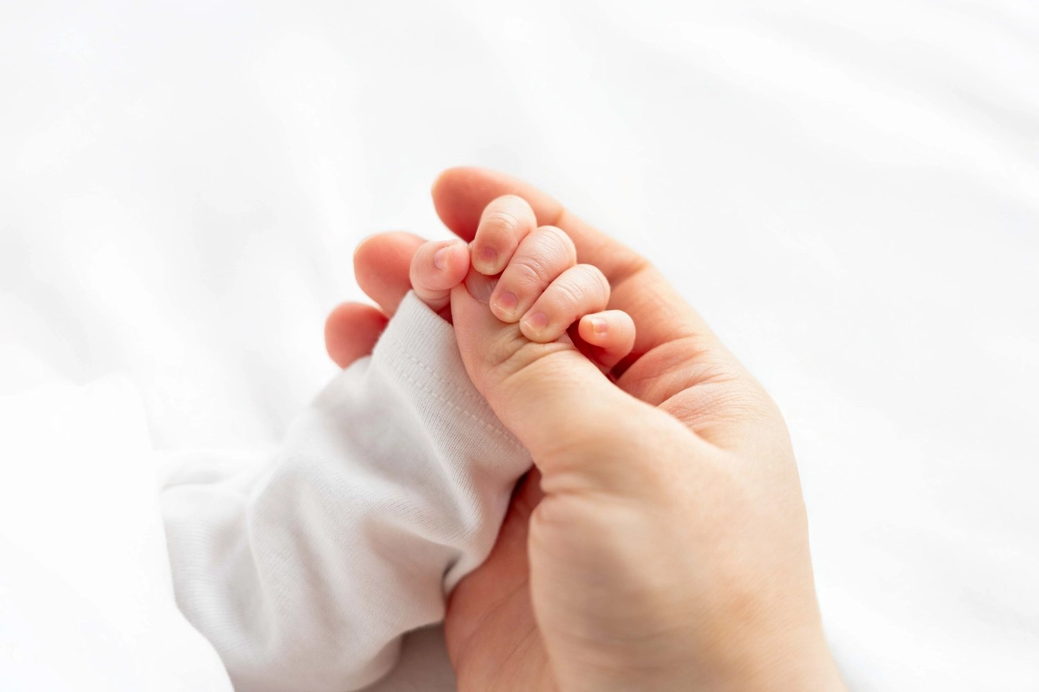 Eine kleine Babyhand umfasst zärtlich den Finger einer erwachsenen Hand.