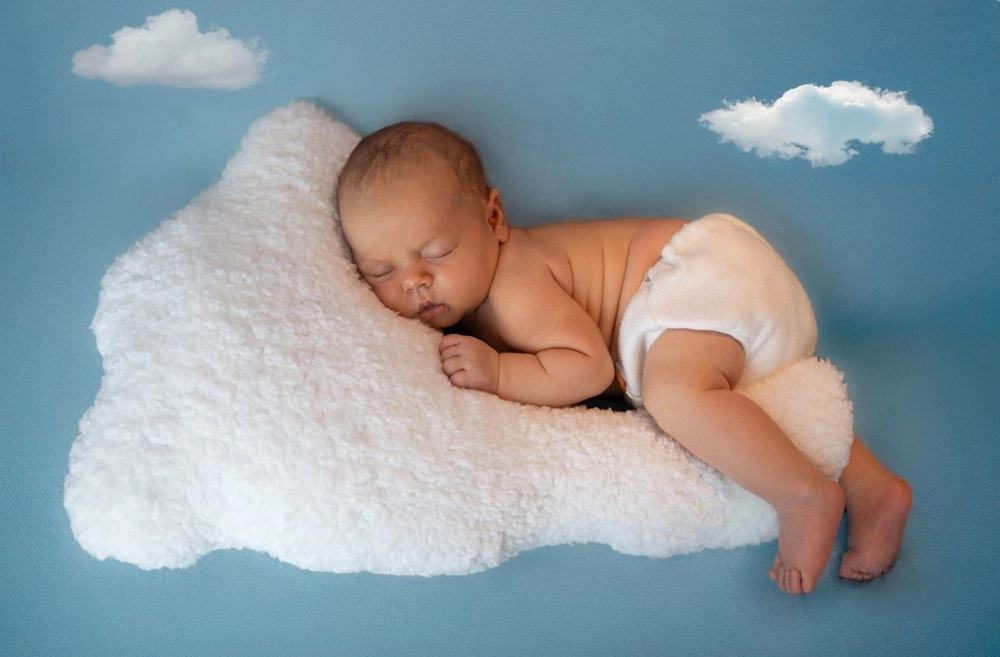 Ein schlafendes Baby liegt auf einer weißen Wolke vor Blau.