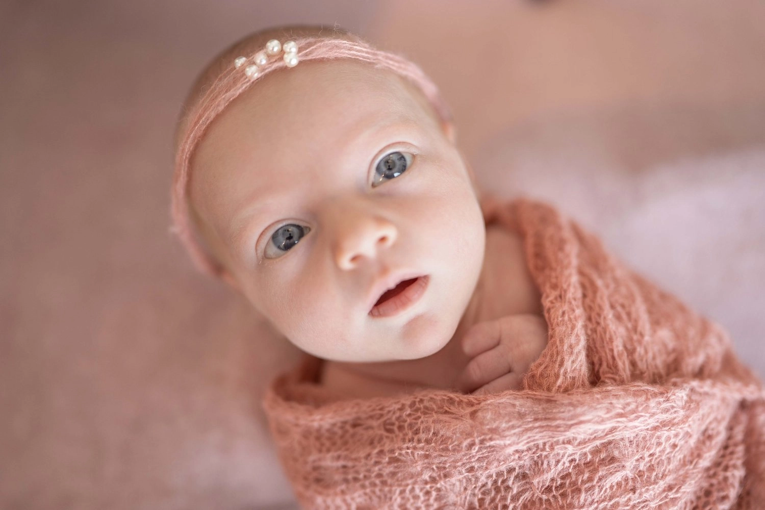 Ein waches Baby mit schmalem Haarband ist in rosa Strick gehüllt.