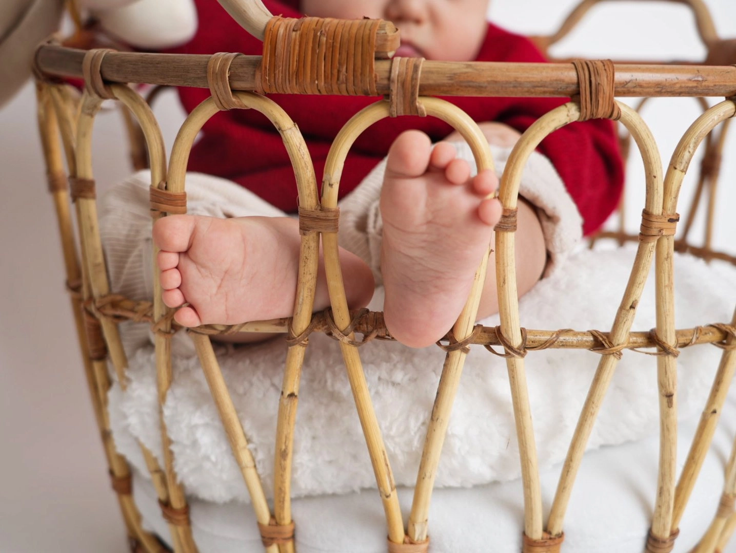 Kleine Babyfüße lehnen am geflochtenen Rand eines weich ausgelegten Korbs.