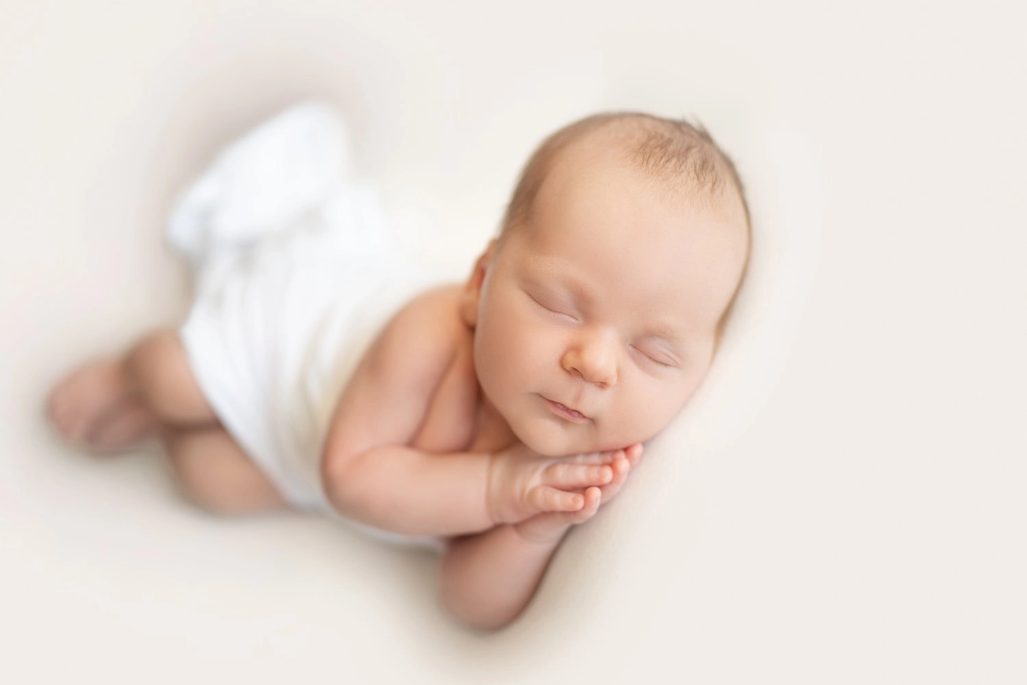 Ein schlafendes Baby in weißer Kleidung legt den Kopf auf seine Hände.