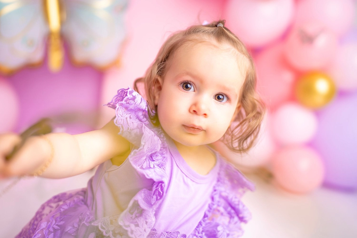 Ein Kind im lilafarbenen Kleid blickt vor Ballons zur Kamera.