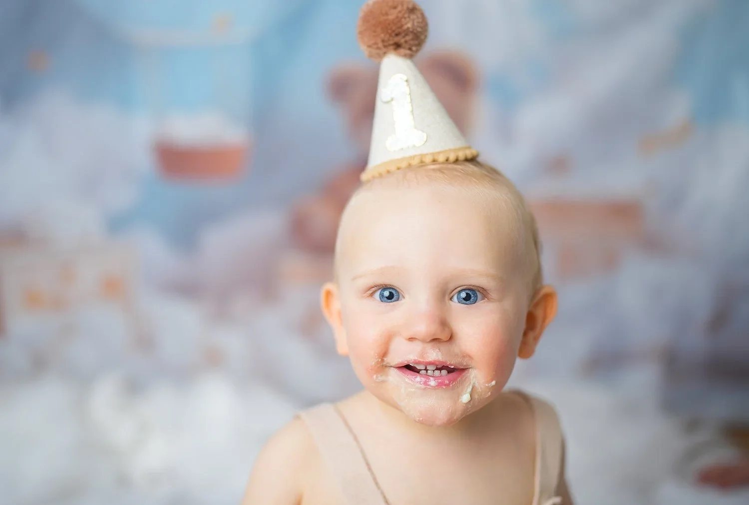 Ein Baby mit kleinem Geburtstagshütchen lächelt mit Tortencreme am Mund.
