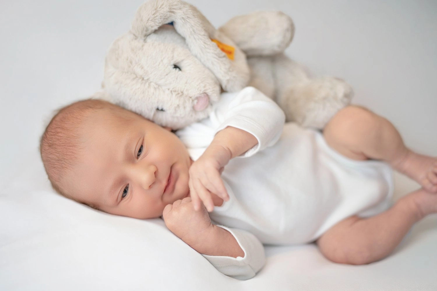 Ein schlafendes Baby liegt in weißer Kleidung neben einem Kuscheltier.