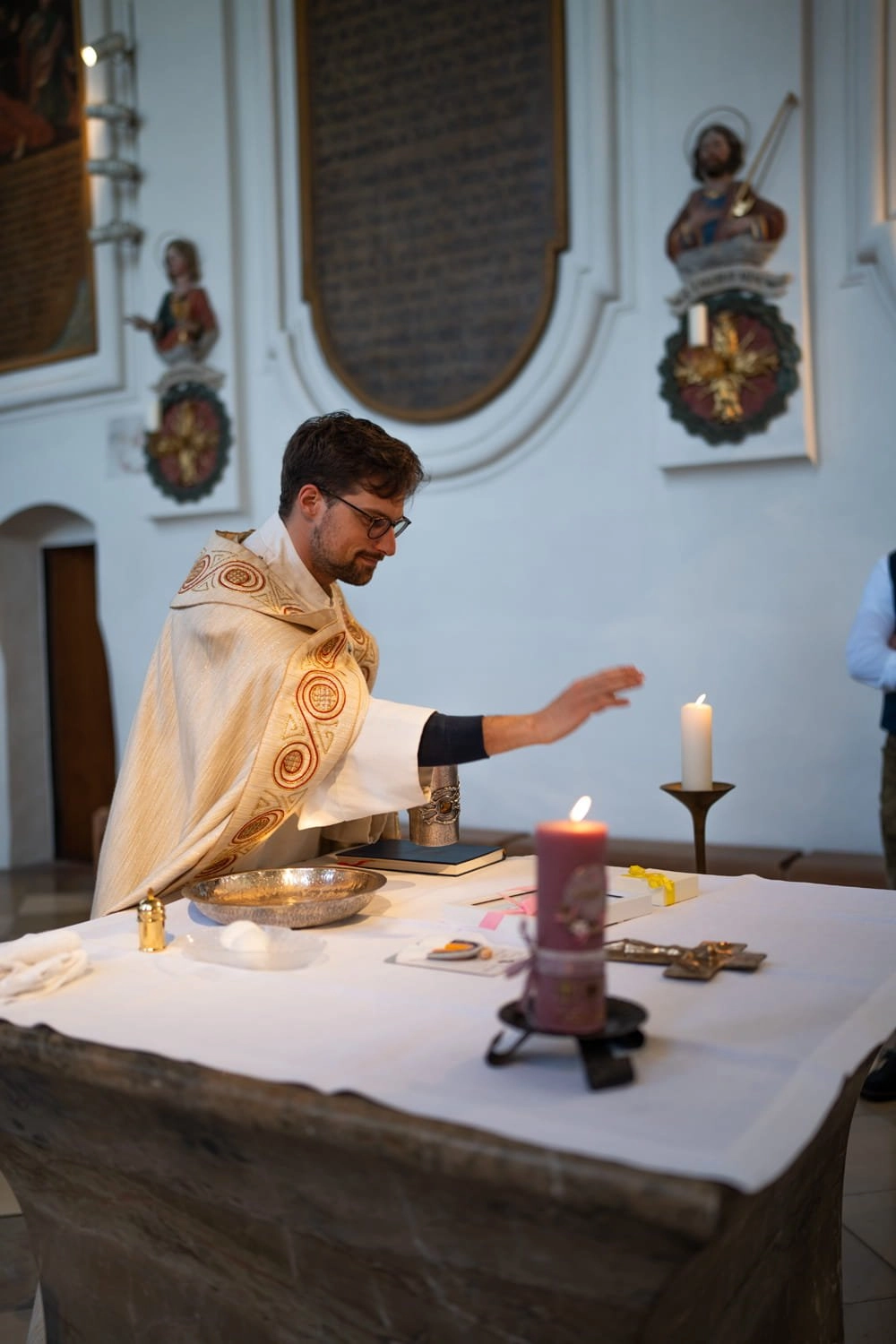 Ein Pfarrer steht am Altar zwischen Kerzen und einem geöffneten Buch.