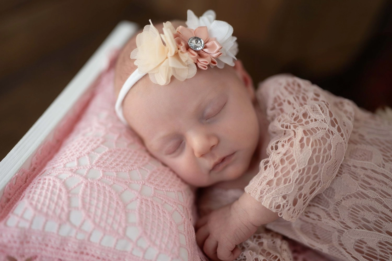 Ein schlafendes Baby mit Blumenhaarband liegt eingekuschelt in einer rosa Decke.