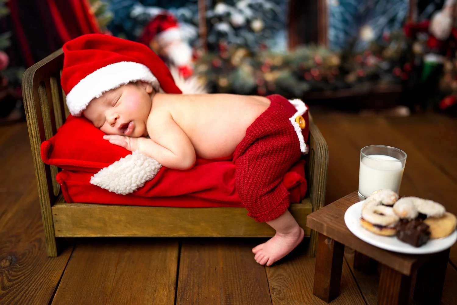 Ein schlafendes Baby mit Weihnachtsmütze liegt neben Milch und Gebäck.