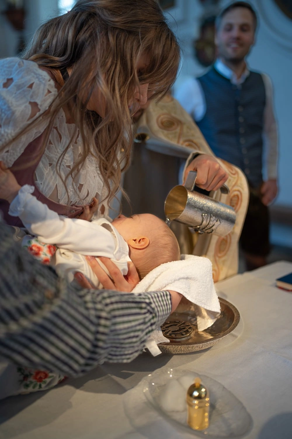 Ein Baby wird am Taufbecken gehalten, während eine Frau darübersteht.