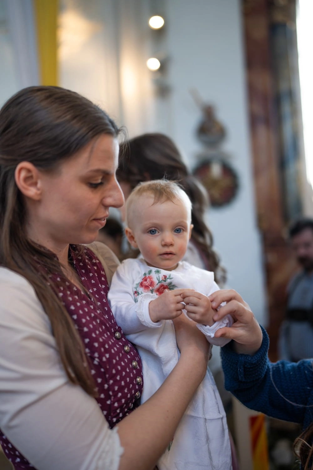 Eine Frau hält ein Baby vor der dekorierten Wand einer Kirche.