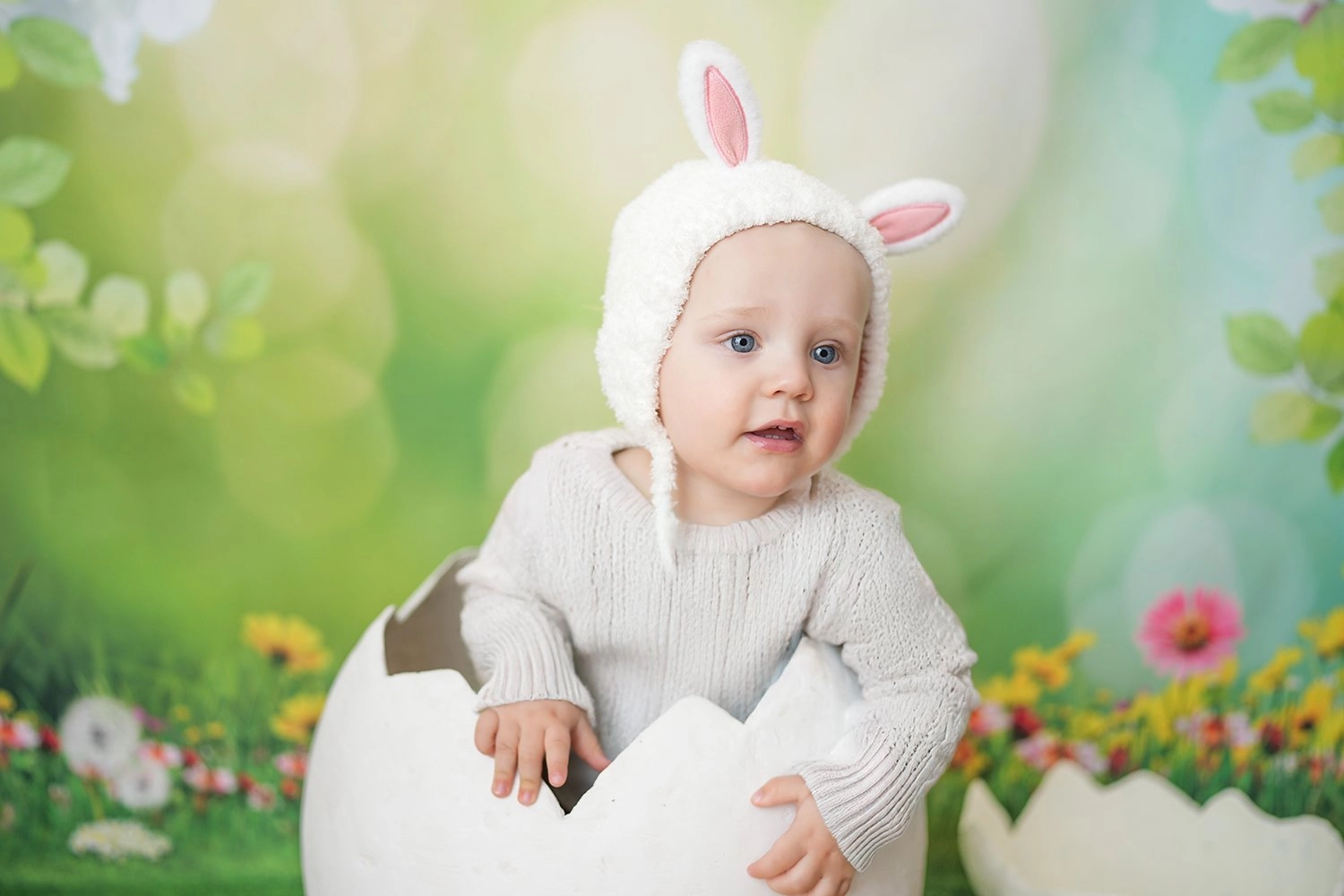 Ein Baby mit weißen Hasenohren sitzt im Dekoei vor Grün.