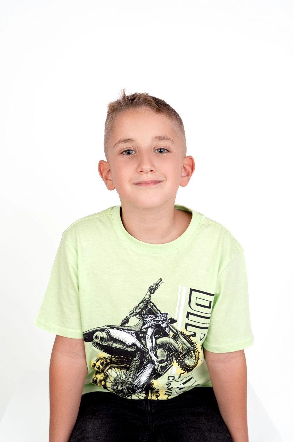 Ein Junge im hellgrünen T-Shirt lächelt vor einem weißen Hintergrund.