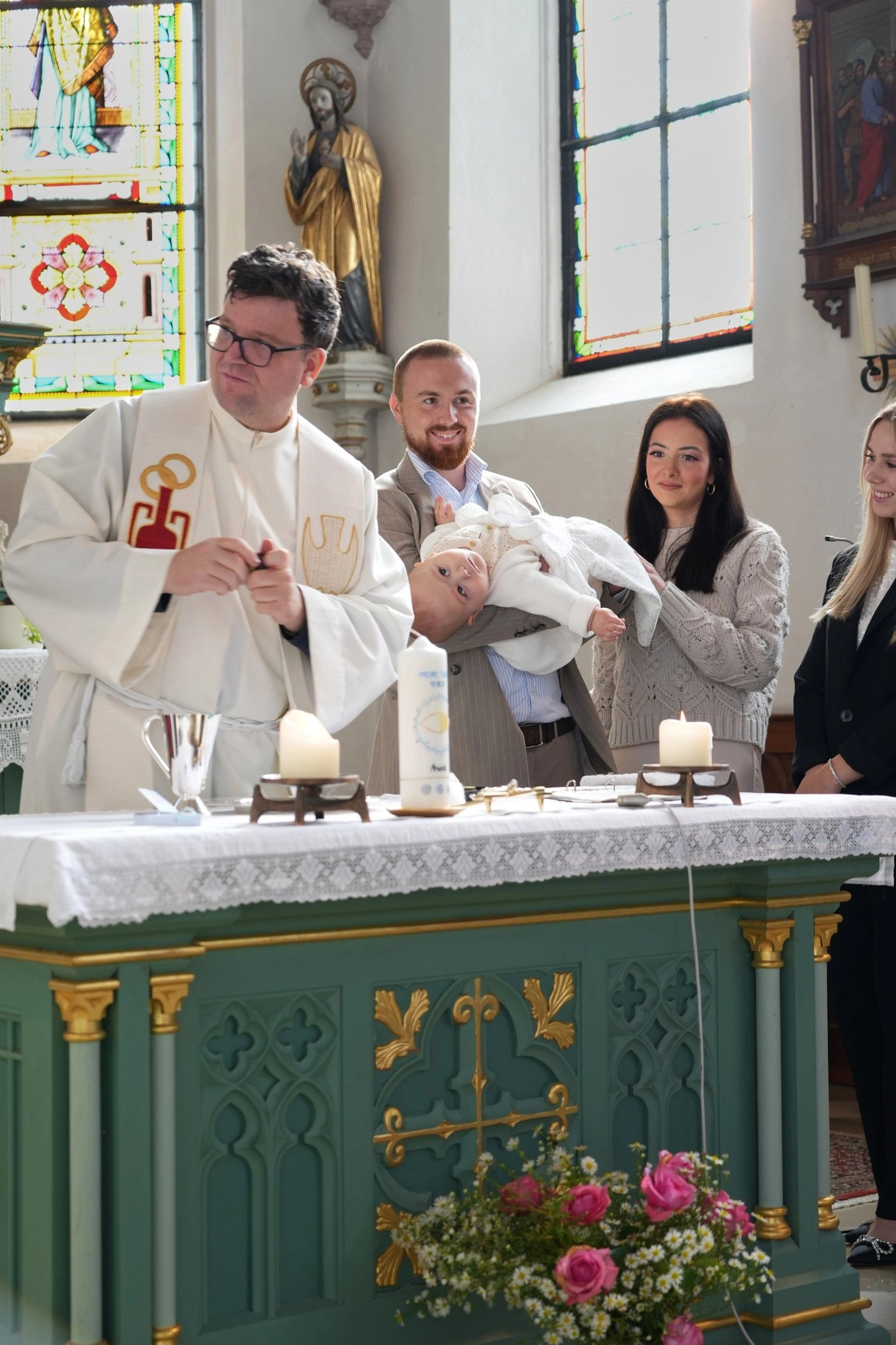 Ein Pfarrer und eine Familie mit Baby stehen hinter dem Kirchenaltar.