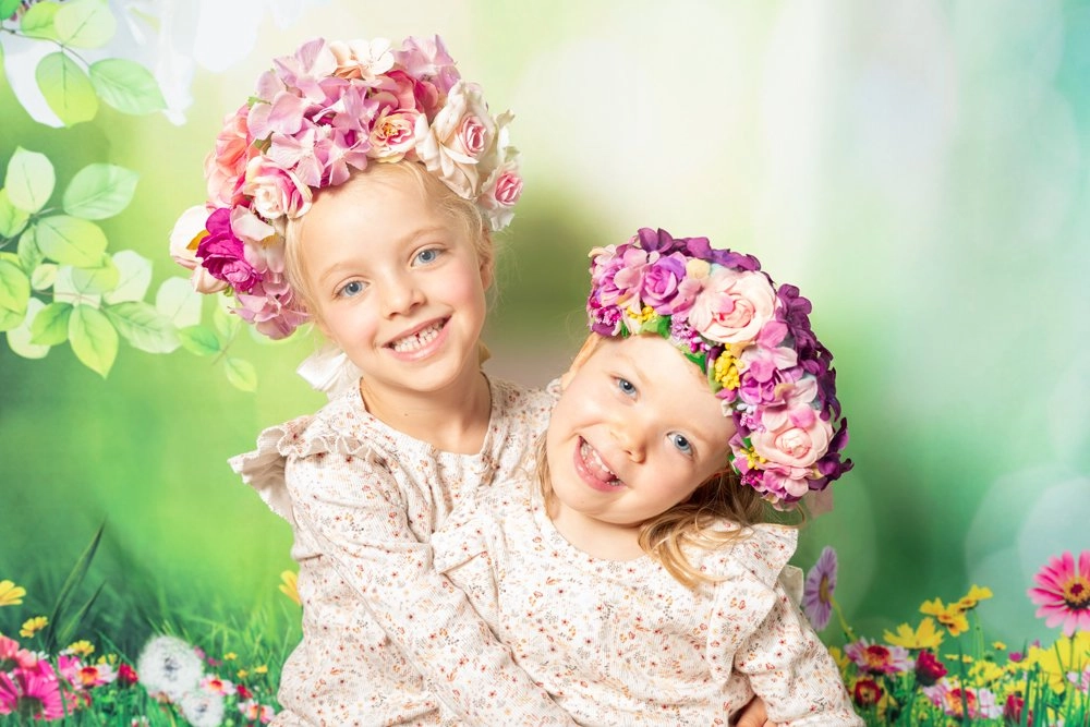 Zwei Kinder mit bunten Blumenkränzen lehnen lächelnd ihre Köpfe zusammen.