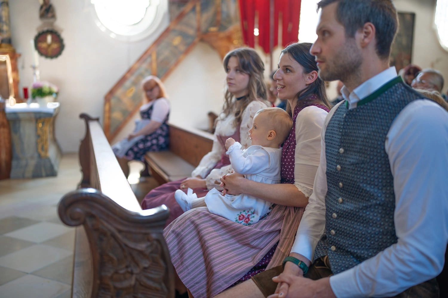 Eine Familie mit Baby sitzt gemeinsam auf einer Kirchenbank.
