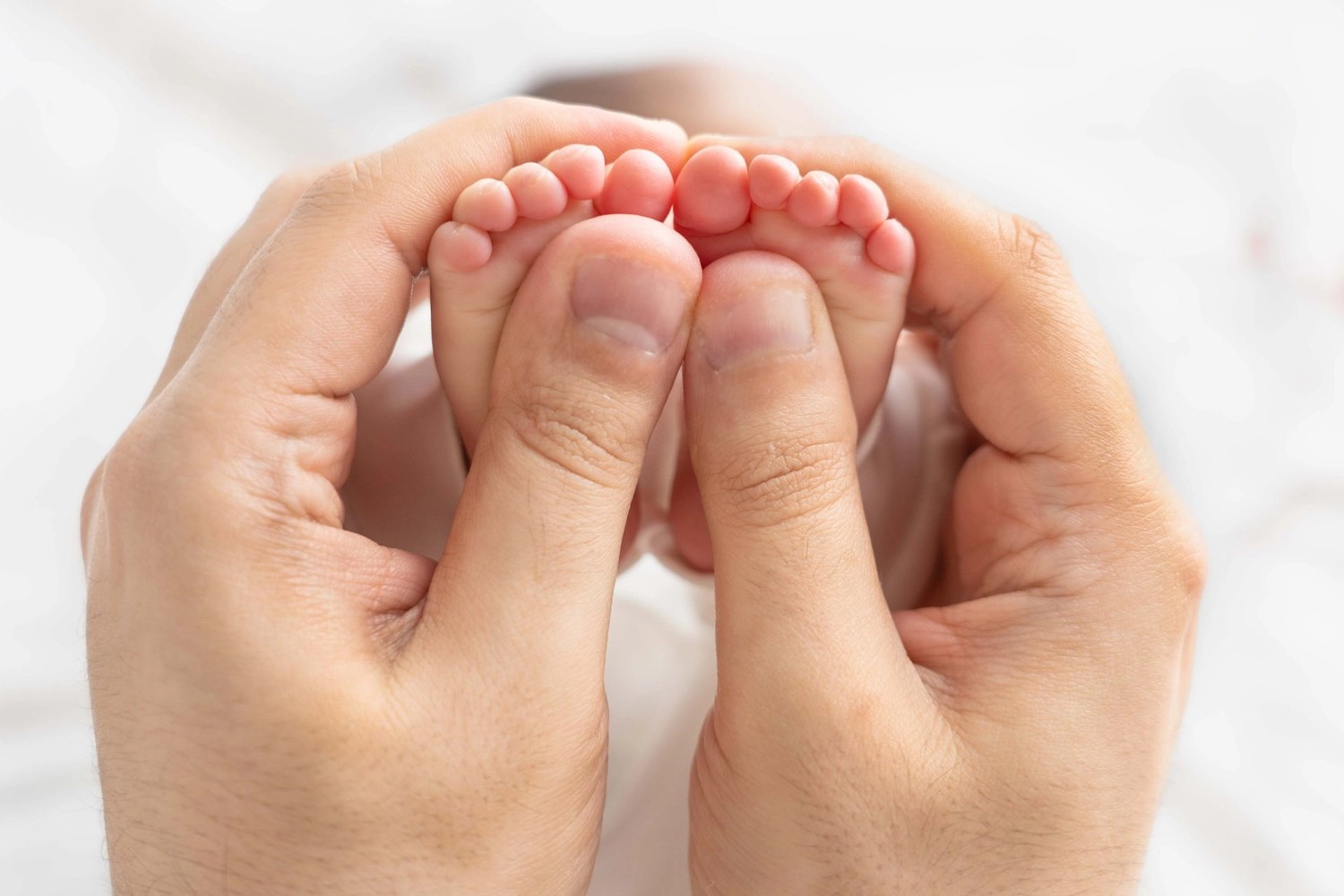 Zwei erwachsene Hände halten behutsam die kleinen Füße eines Babys.