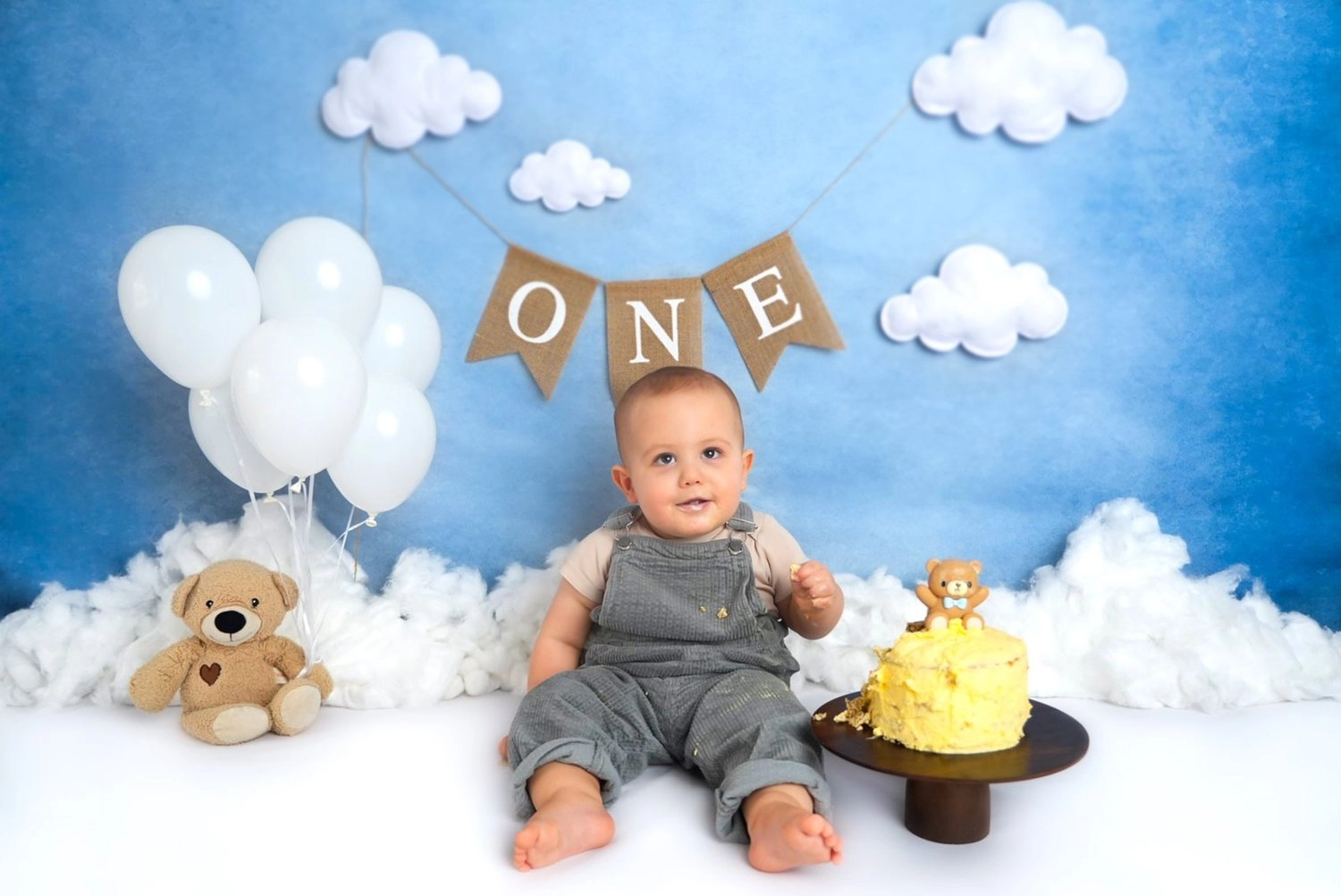 Ein Baby sitzt neben einer Torte vor einer One-Girlande und Wolken.