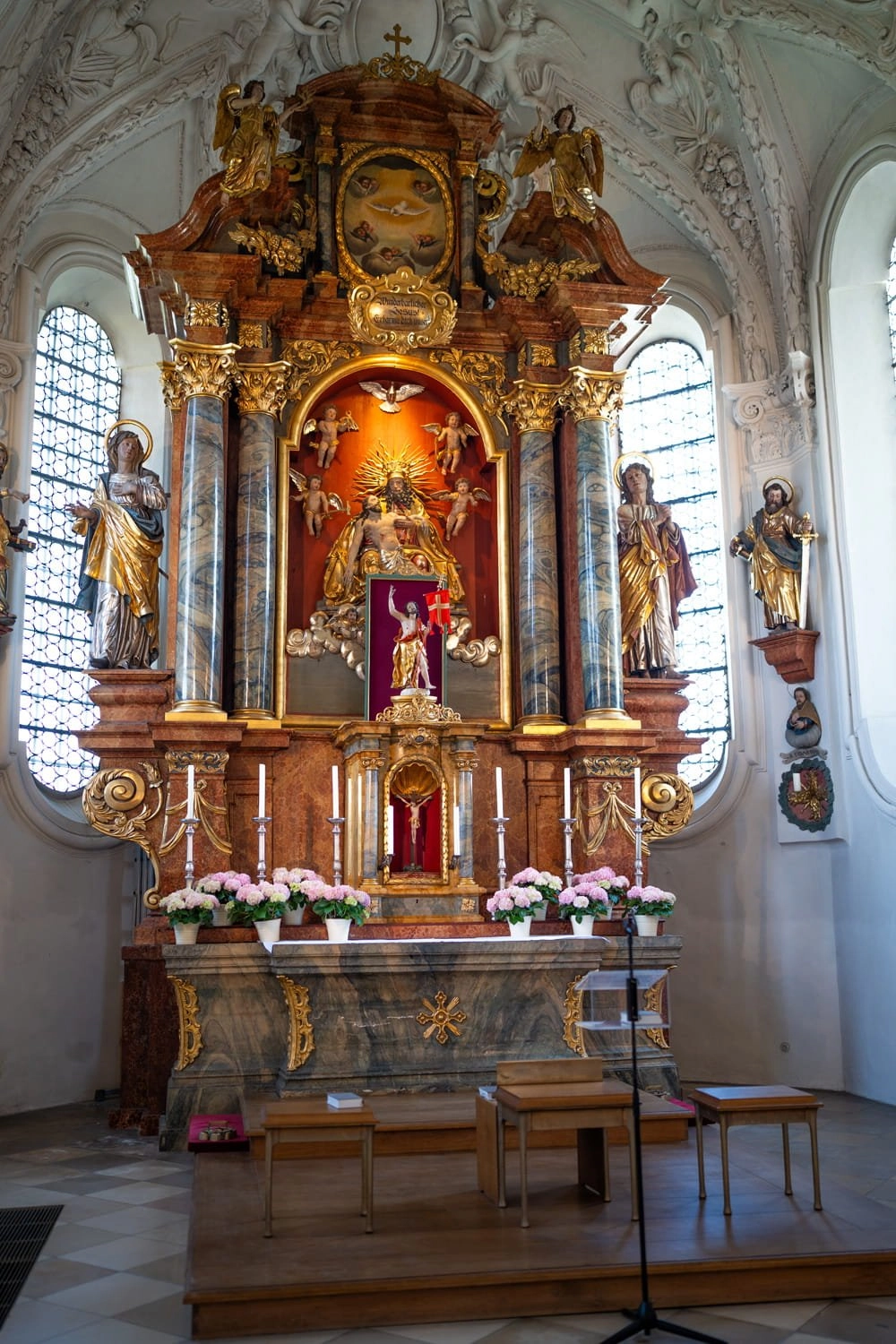 Ein reich verzierter Kirchenaltar steht zwischen hohen Fenstern im Kirchenraum.
