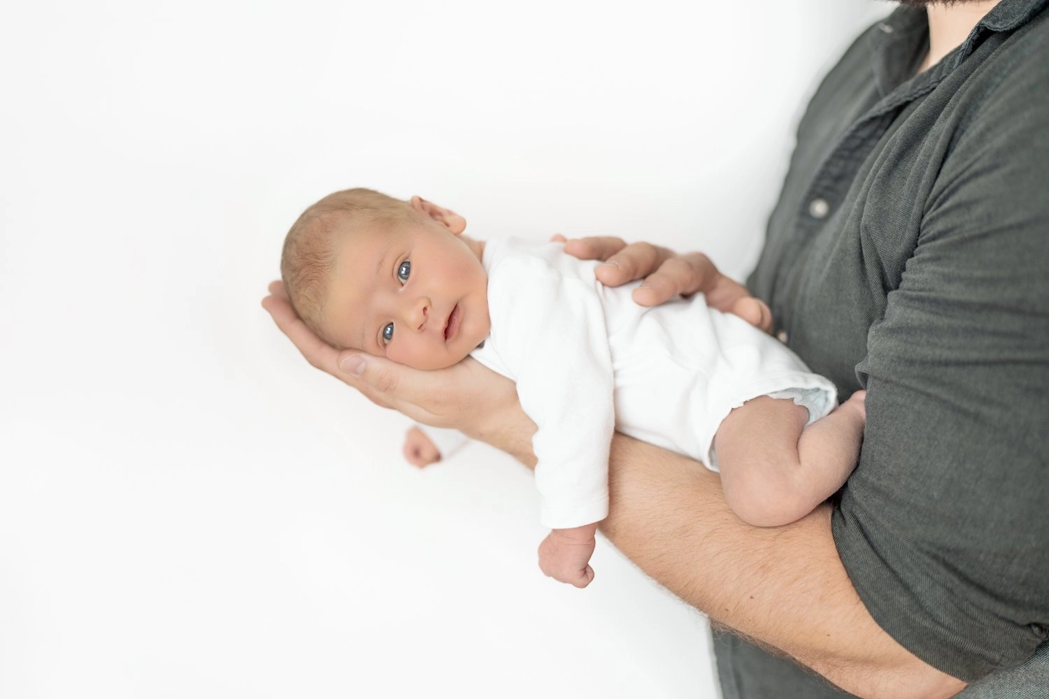 Ein waches Baby in weißer Kleidung liegt im Arm eines Erwachsenen.