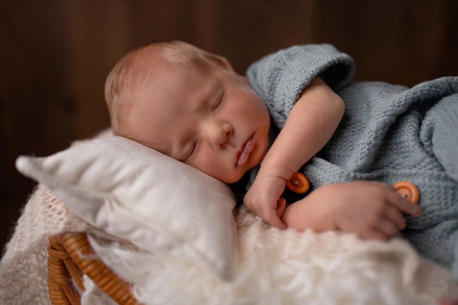 Ein Baby im blauen Outfit schläft auf einem weichen weißen Kissen.