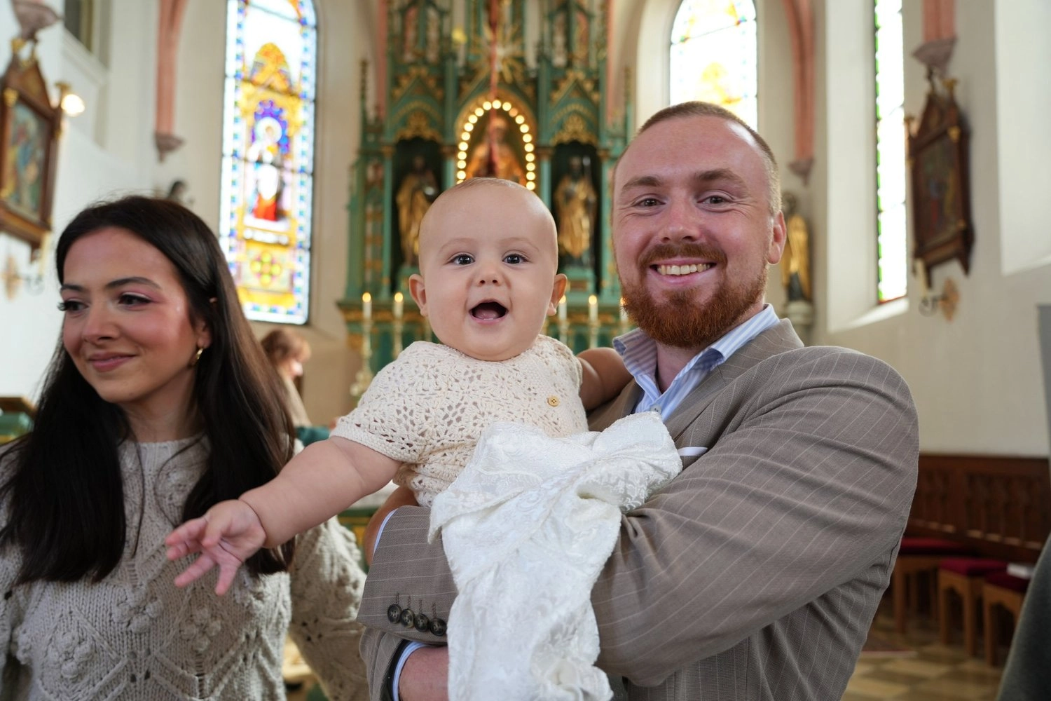 Eine Familie mit Baby lächelt gemeinsam während einer Feier in der Kirche.
