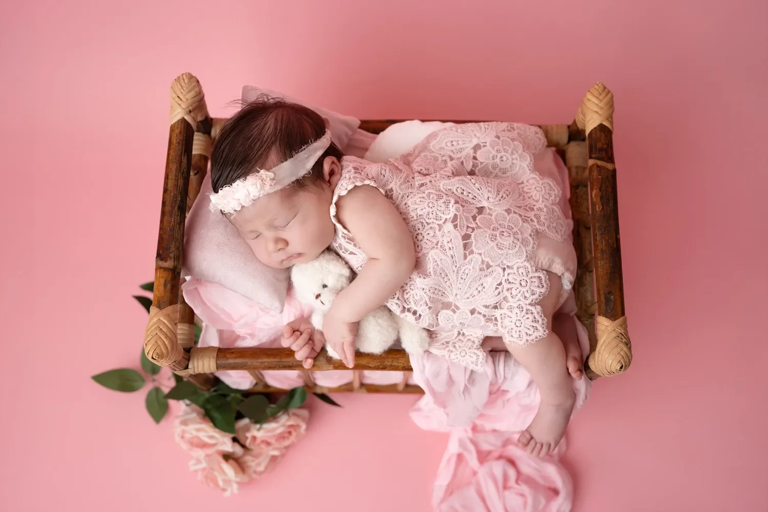 Ein schlafendes Baby liegt im kleinen Holzbettchen auf rosa Untergrund.
