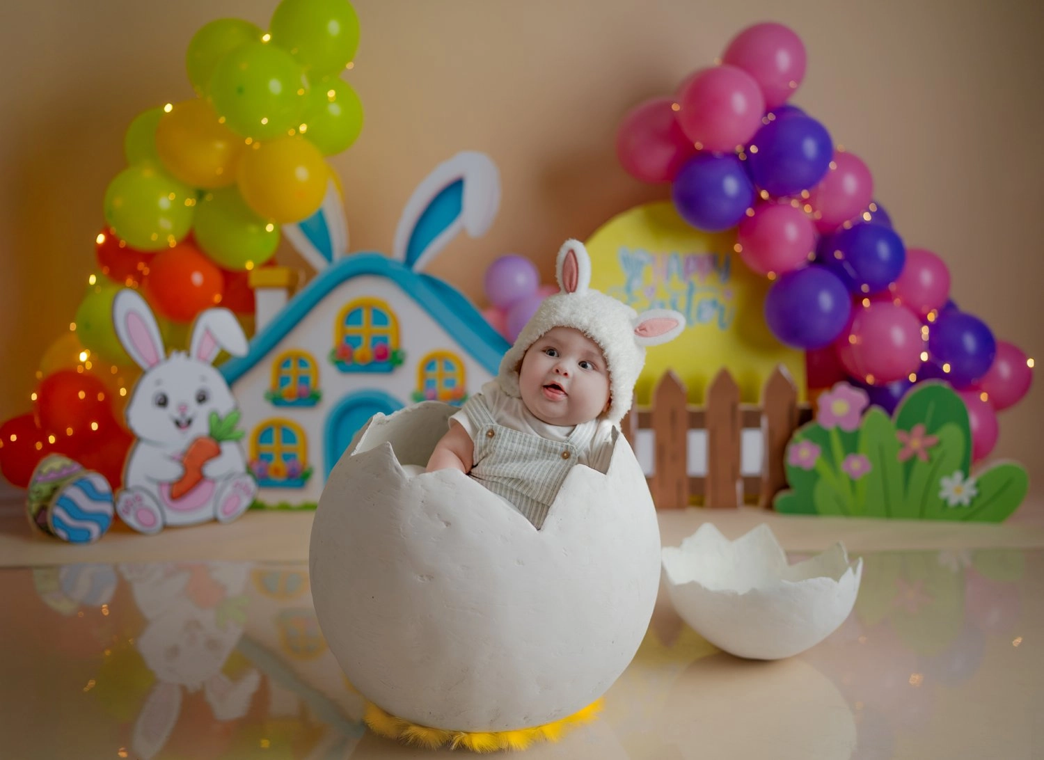 Ein Baby mit Hasenohren sitzt im Dekoei vor bunten Ballons.