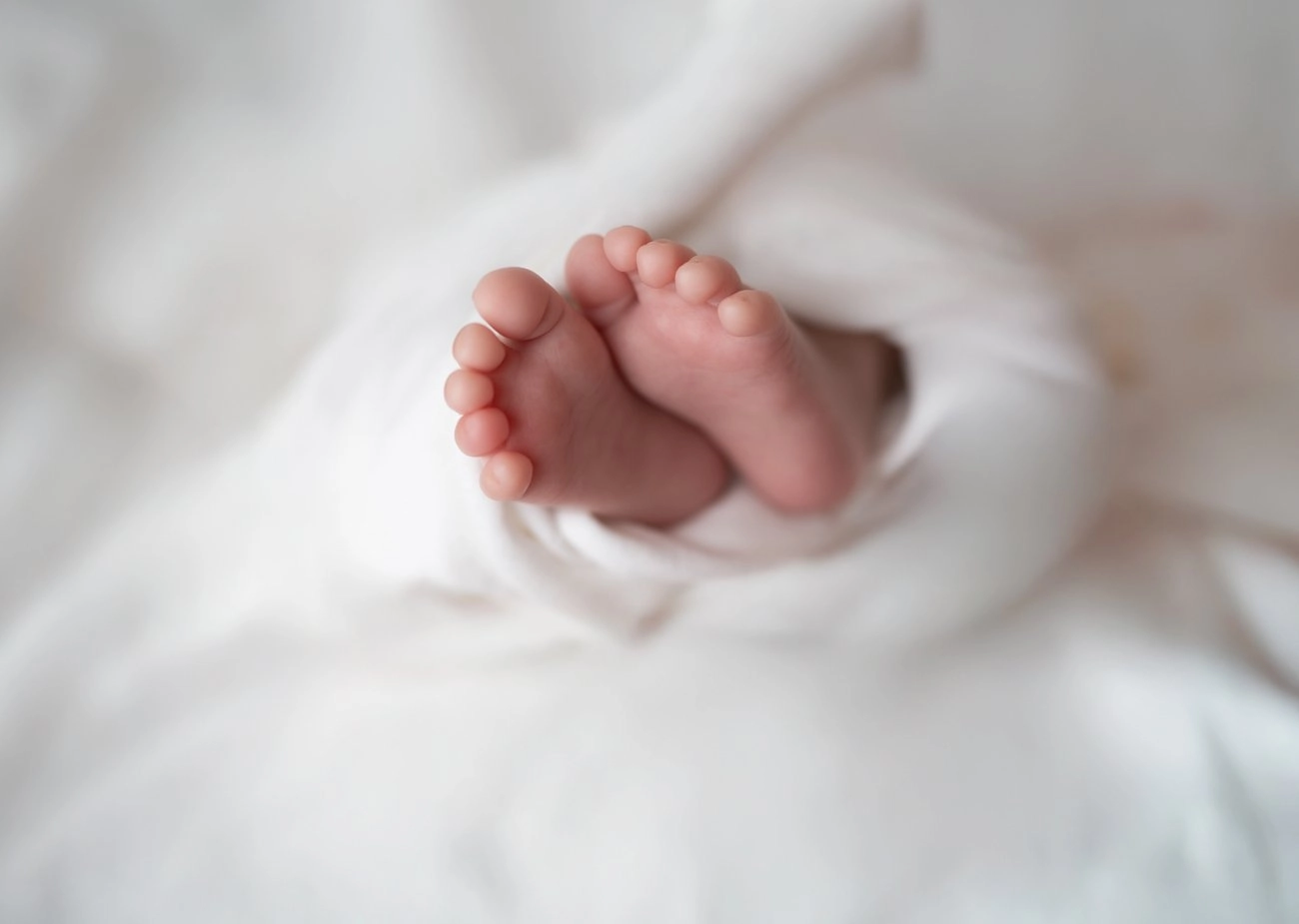 Kleine Babyfüße schauen zwischen weichem weißen Stoff hervor.