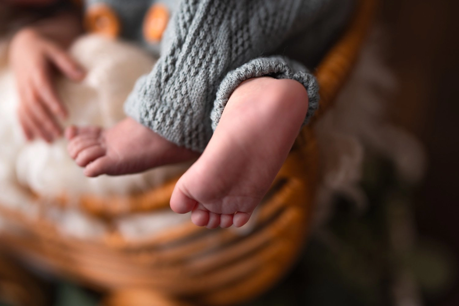 Kleine Babyfüße ragen unter blauem Strick über den Körbchenrand.