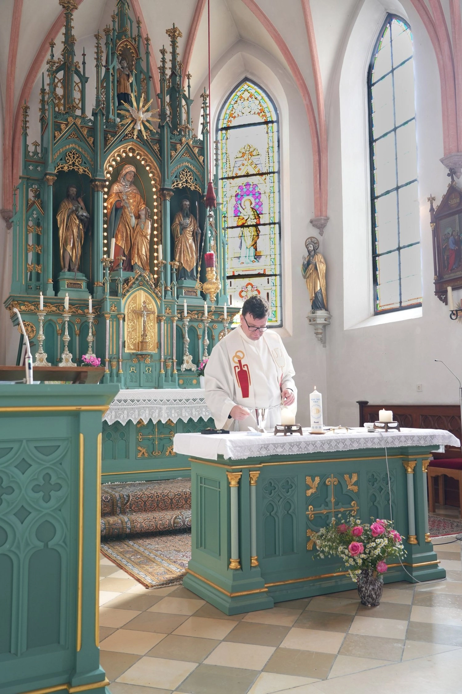 Ein Pfarrer steht am geschmückten Taufbecken vor dem Kirchenaltar.