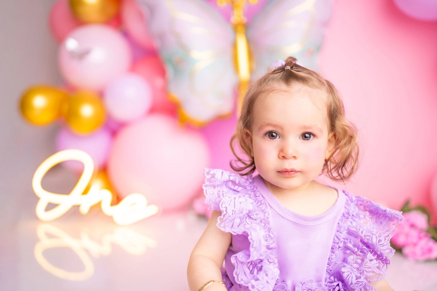 Ein Kind im lilafarbenen Kleid sitzt aufmerksam vor bunten Geburtstagsballons.