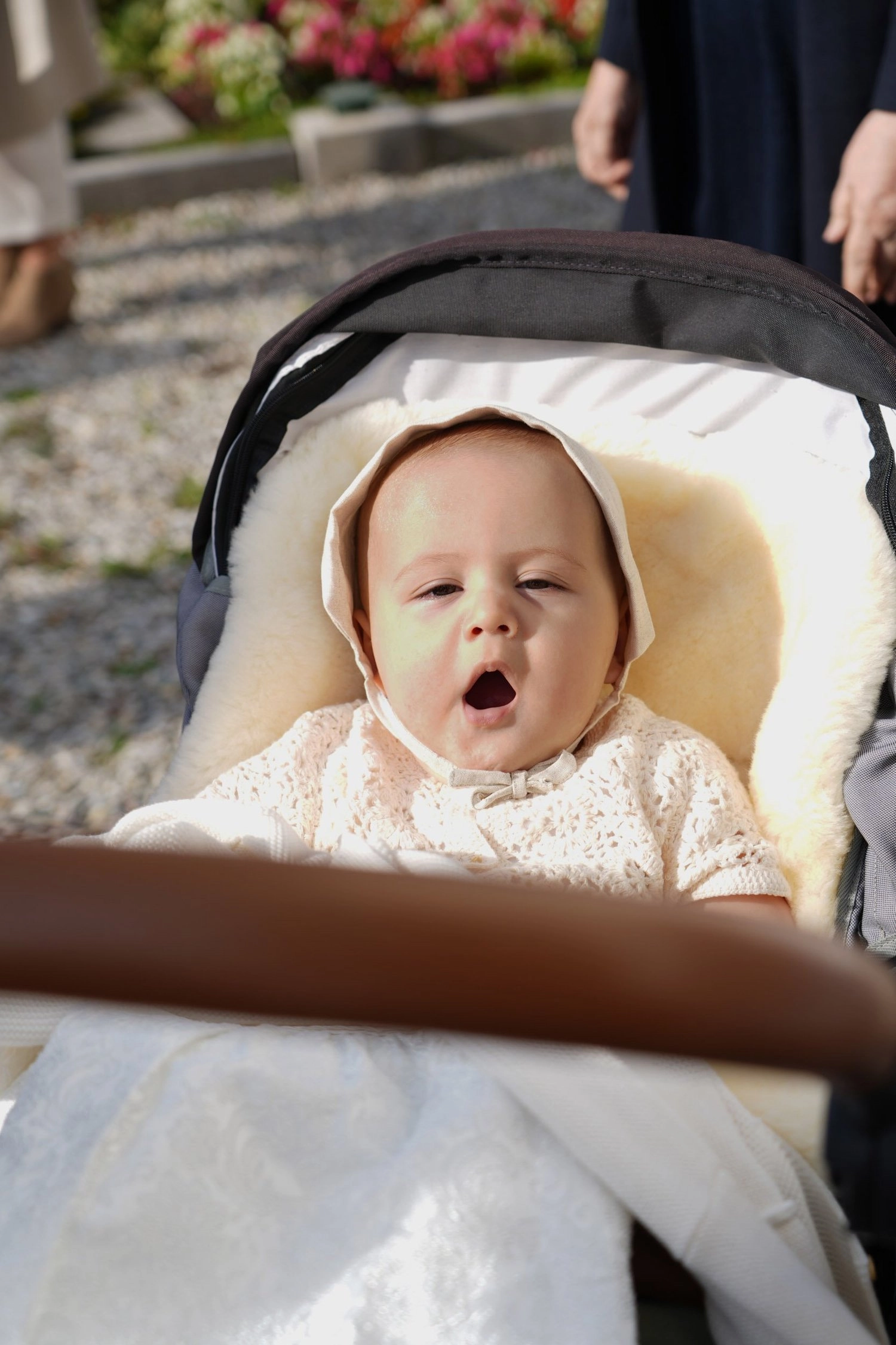 Ein Baby mit heller Haube liegt gähnend in seinem Kinderwagen.