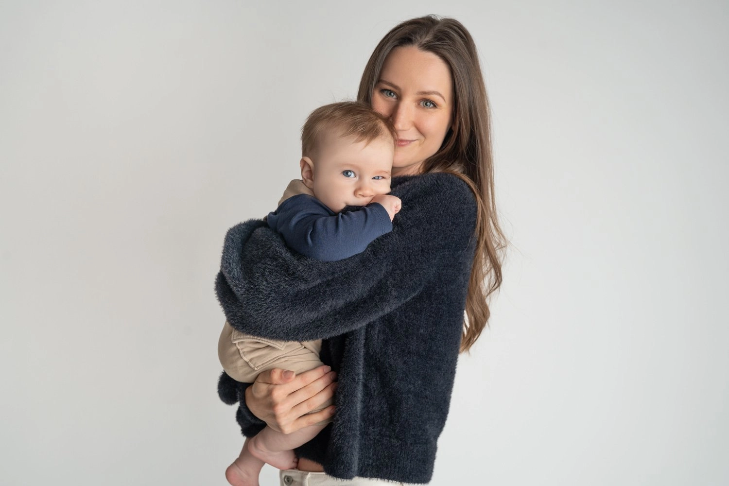 Eine Frau im dunklen Pullover kuschelt mit einem Baby im Arm.