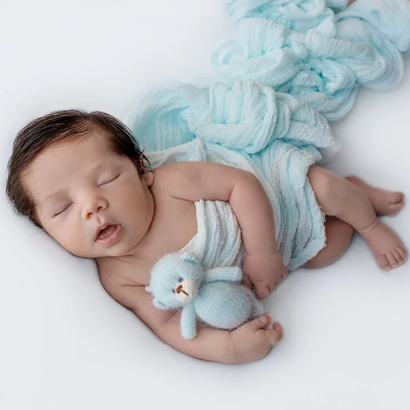 Ein schlafendes Baby liegt mit Häkelhase neben hellblauen Stoffblüten.