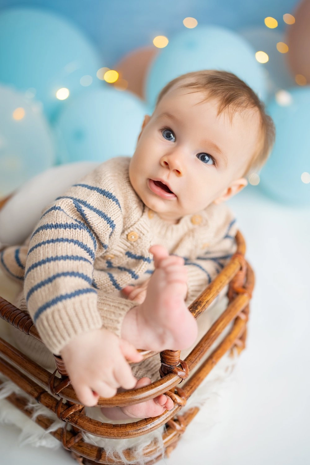 Ein Baby im Streifenpullover hält seinen Fuß im kleinen Körbchen.