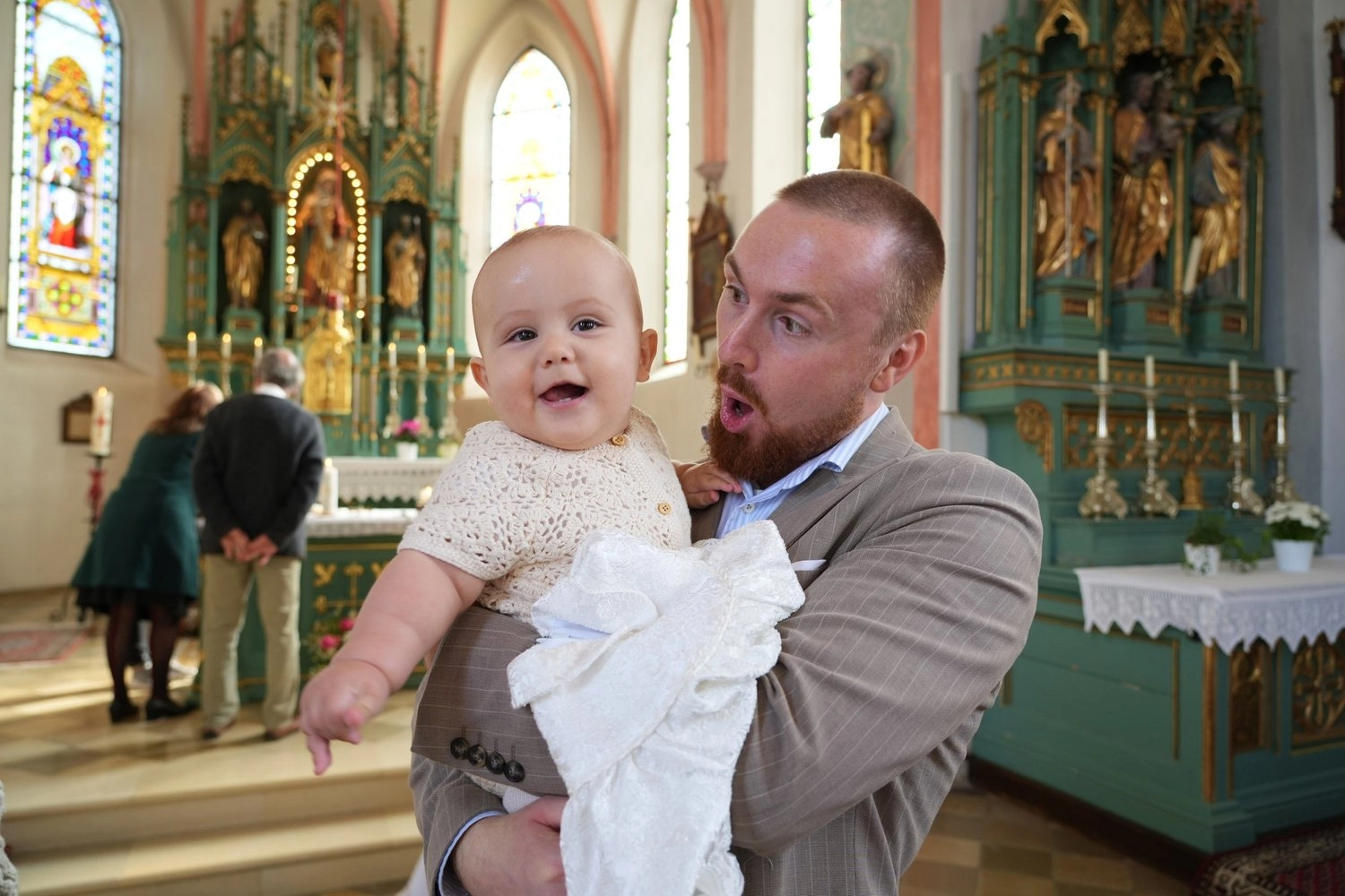 Ein Mann hält ein lachendes Baby vor dem geschmückten Kirchenaltar.