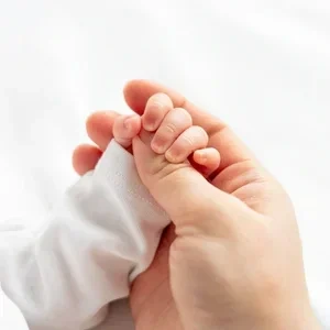 Kleine Babyfinger umklammern einen erwachsenen Finger vor einem weißen Hintergrund.