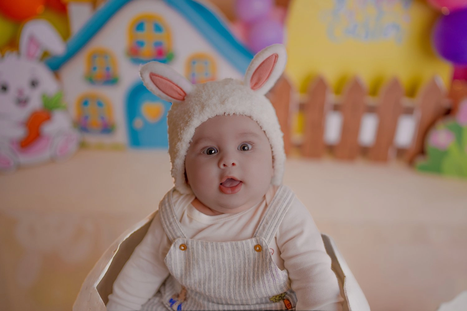 Ein Baby mit Hasenmütze sitzt vor einer farbenfrohen Osterlandschaft.