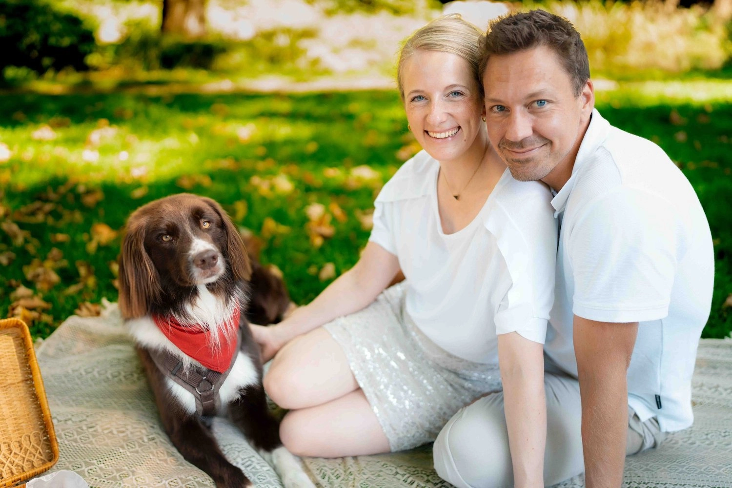 Ein lächelndes Paar sitzt mit seinem Hund auf einer grünen Wiese.