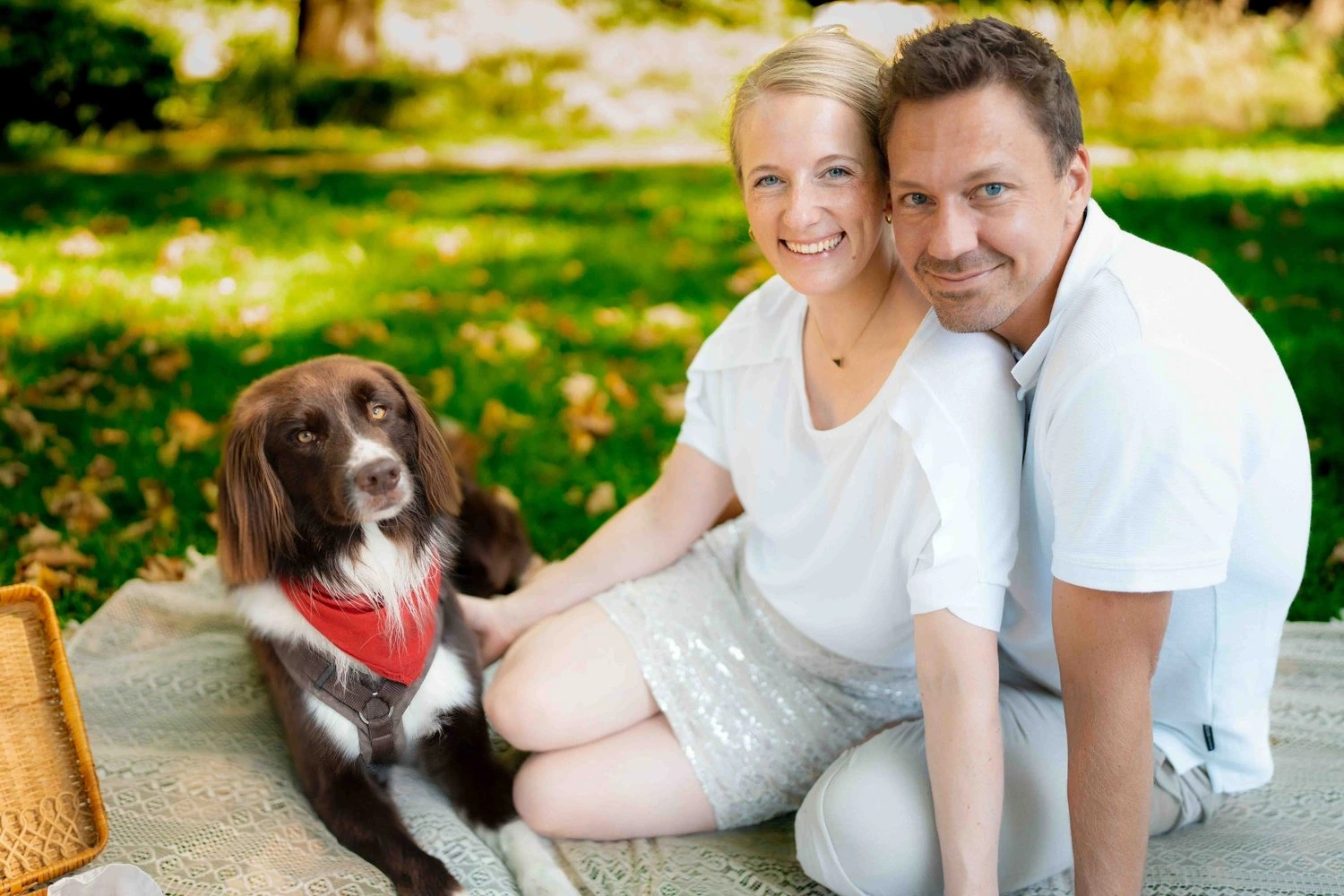 Ein lächelndes Paar sitzt mit seinem Hund auf einer grünen Wiese.