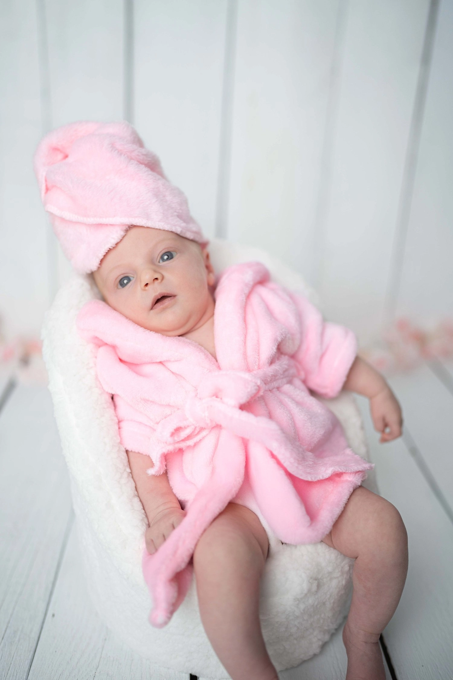 Ein waches Baby trägt einen rosa Bademantel und ein passendes Handtuch.
