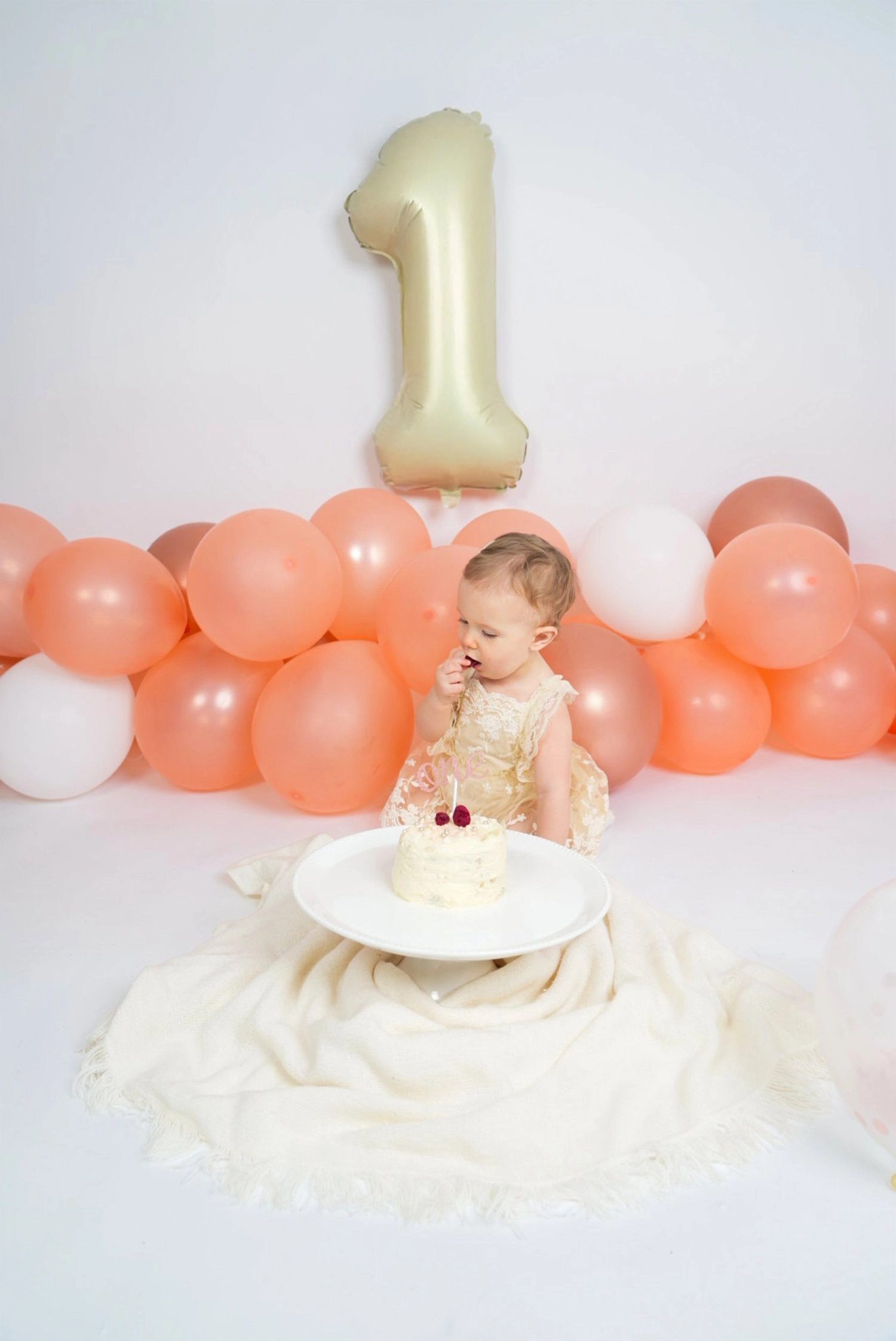 Ein kleines Kind sitzt mit seiner Torte unter einem goldenen Einserballon.