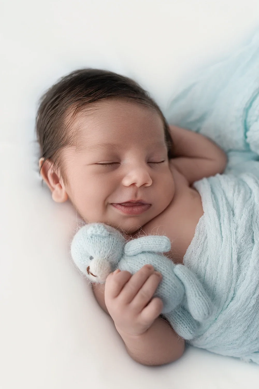 Ein schlafendes Baby hält einen Häkelhasen auf einem hellen Untergrund.